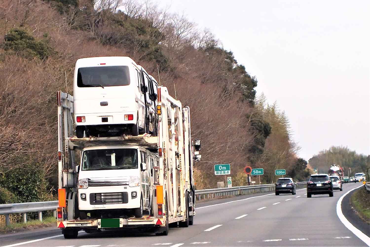 ナンバー無しのクルマを運搬するキャリアカーが高速道路を走行しているイメージ写真 〜 画像1