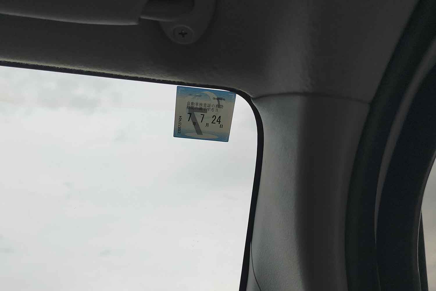 自動車の車検シールがフロントウィンドウガラスの端に貼られている写真