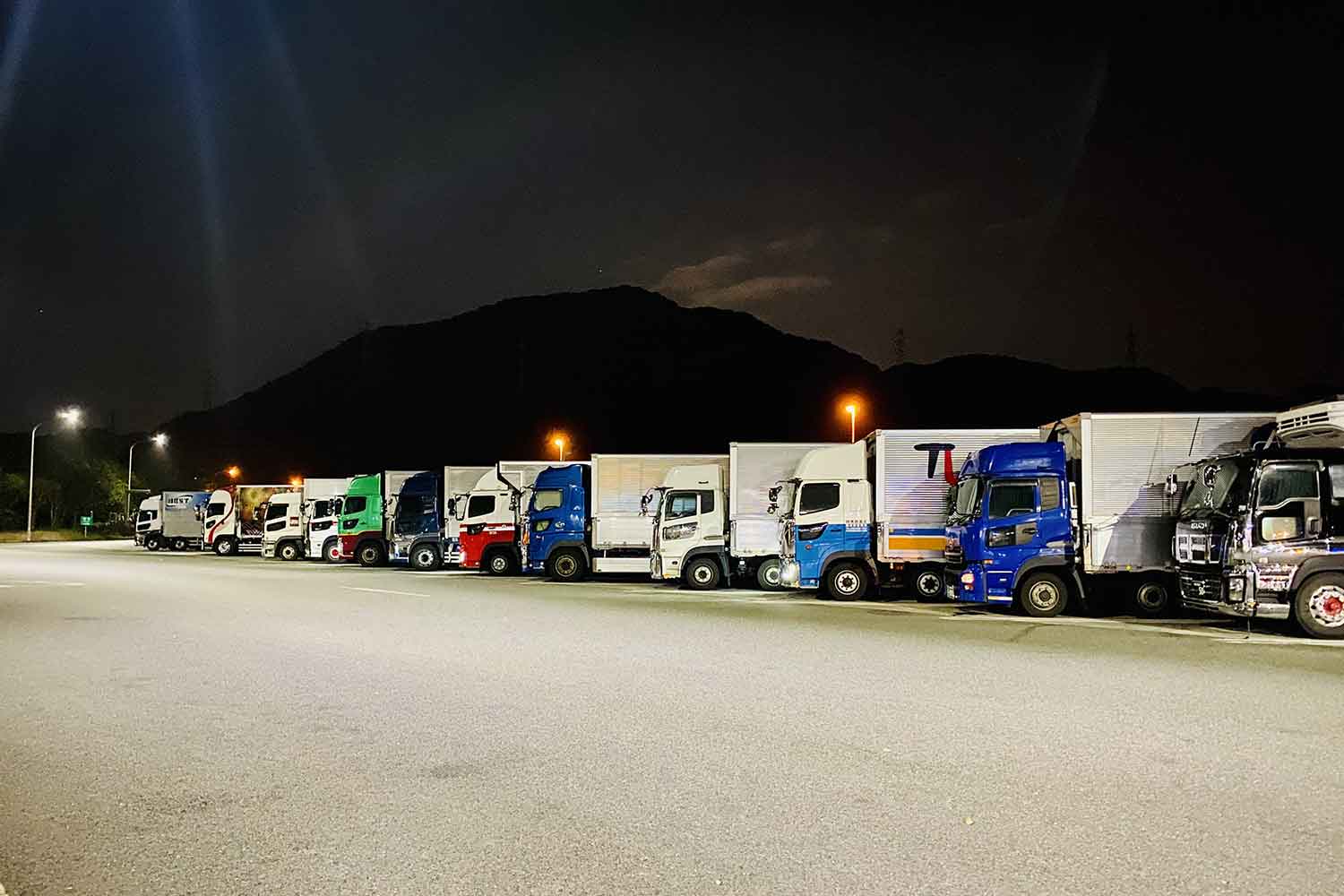 夜間のサービスエリアに駐車している複数台の大型トラック